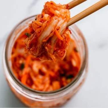 Bowl of homemade kimchi featuring vibrant red peppers and fresh vegetables.