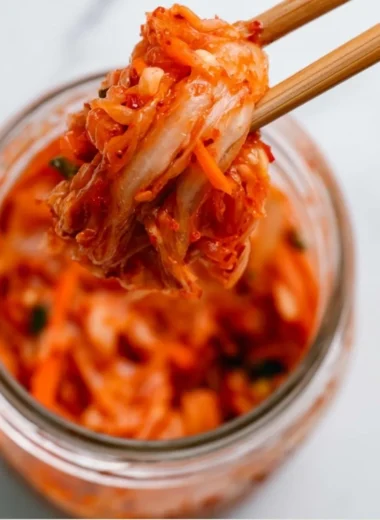 Bowl of homemade kimchi featuring vibrant red peppers and fresh vegetables.